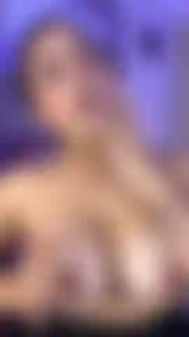 A sweet brunette beauty kneels on the bed to rub and suck her big tits