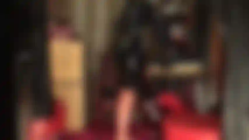 Glänzendes latex-outfit, strümpfe und maske – die göttin zeigt ihre kurven in engem latex, transparenten nahtstrümpfen und einem schwarzen bleistiftrock mit handschuhen. Das outfit wird durch eine latexmaske komplettiert.