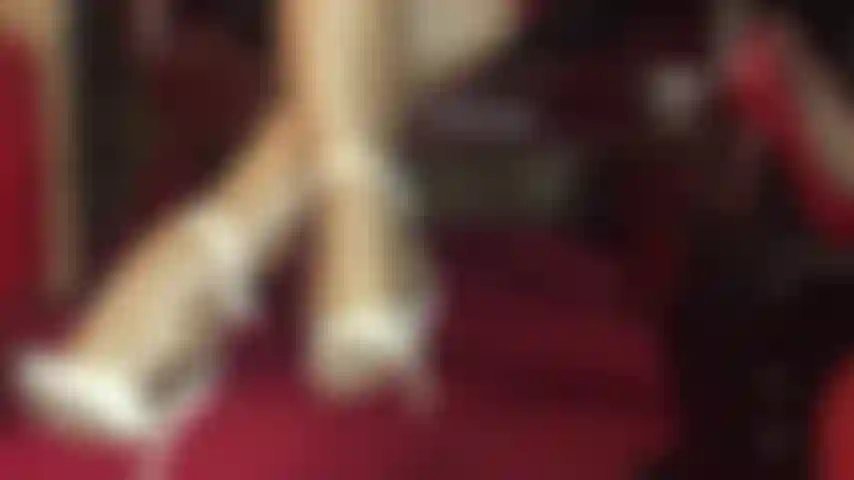 Unglaublich glänzende strumpfhosenbeine in goldenen nylonschichten und weißen sandalen mit knöchelriemen.