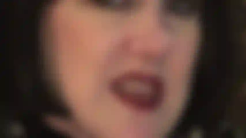 Nahaufnahme des gesichts, schwarze bobperücke, neckisch mit rot geschminkten lippen und feuchter zunge sowie zähnen und händen in lederhandschuhen, die deine hoden gerne festhalten würden.