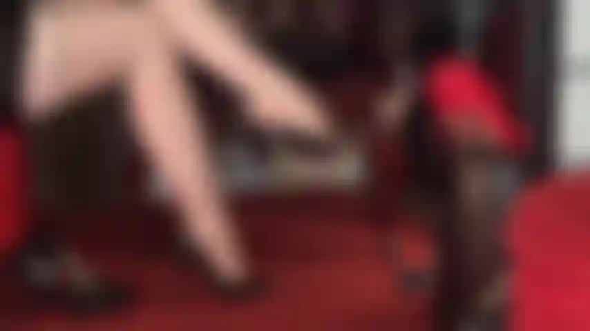 Hautfarbene strumpfhosen mit strumpfbandmuster und nähten, übereinandergeschlagene beine und verführerische füße, an denen verschiedene paare klassischer pumps baumeln.