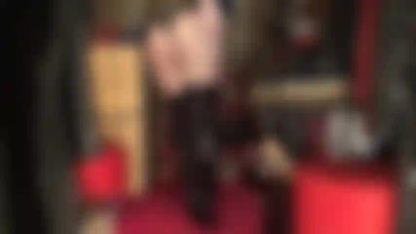 Eine göttin der arschverehrung in einem glänzenden schwarzen pvc-string-bodysuit und hohen stiefeln über schwarzen, durchsichtigen strumpfhosen.