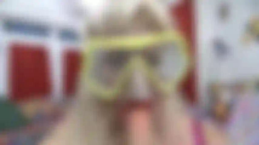 Pov des gesichts mit tauchermaske, die es mit rotem lippenstift beschlägt und an einem weißen spielzeug lutscht.